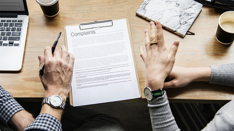 two people sitting at table woman pointing at white complaint form