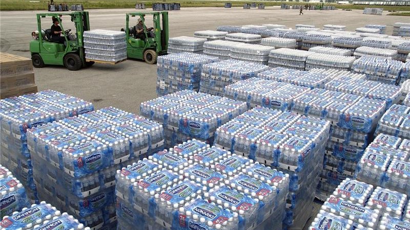 Pallets stacked with cases of bottled water being moved by forklifts