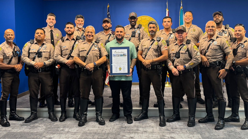 Deputy Joseph Vallejos holds a framed proclamation while surrounded by fellow uniformed deputies
